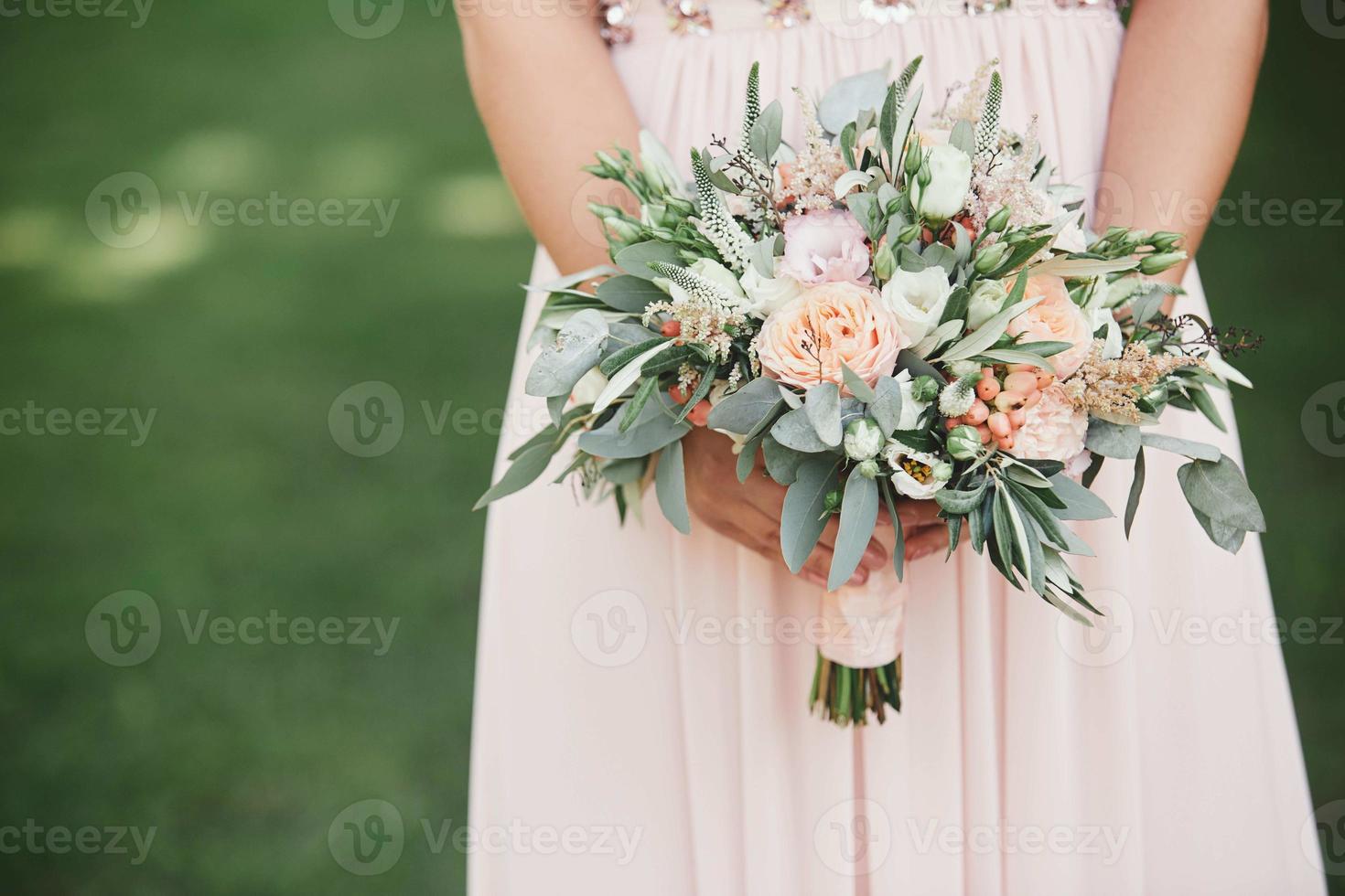 The bride in an elegant wedding dress holds a beautiful bouquet of different flowers and green leaves. Wedding theme photo