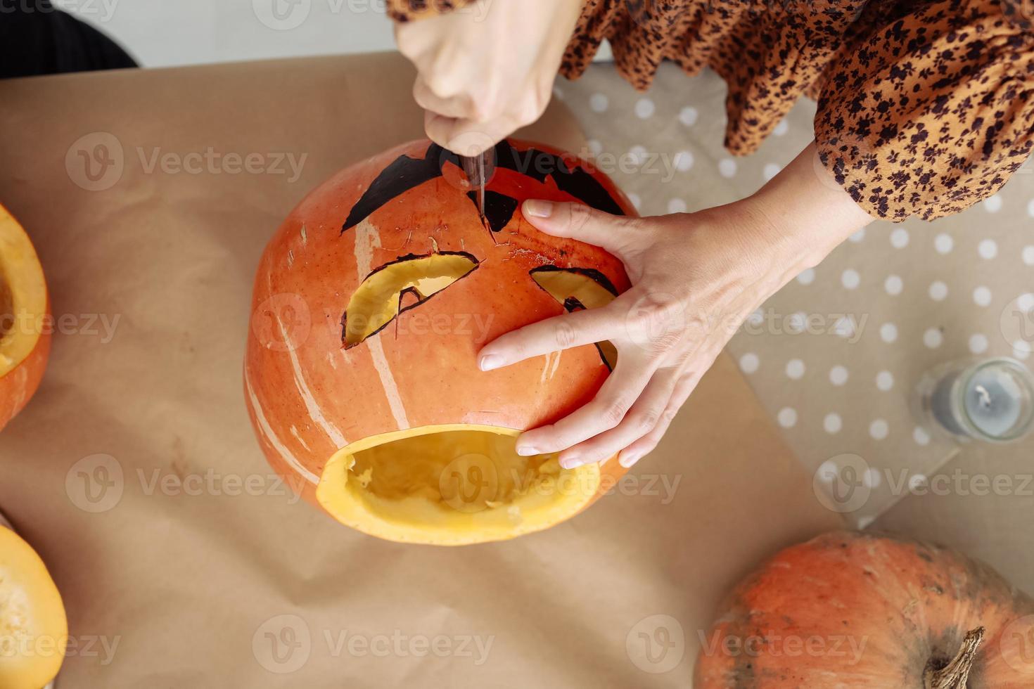 primer plano de una joven tallando jack o latern de calabaza naranja madura con un cuchillo en su mesa de cocina de madera. mujer preparando todas las decoraciones de la fiesta de halloween de la víspera de todos los santos. fondo, copie el espacio. foto