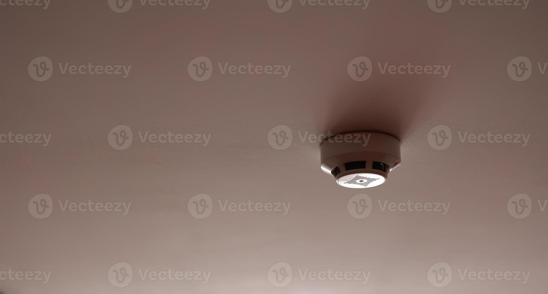 Fire system indoors. White smoke detector issue a signal to a fire alarm control panel as part of a fire alarm system installed on the white ceiling in the office building or apartment. photo