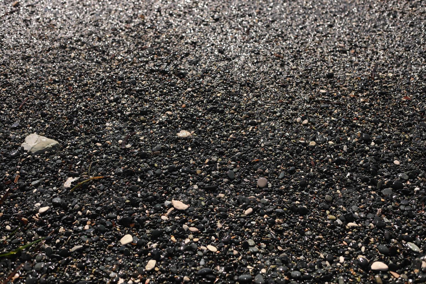 Shallow volcanic black sand beach and pebbles on the sea coast. Ocean shore natural background with copy space. selective focus photo
