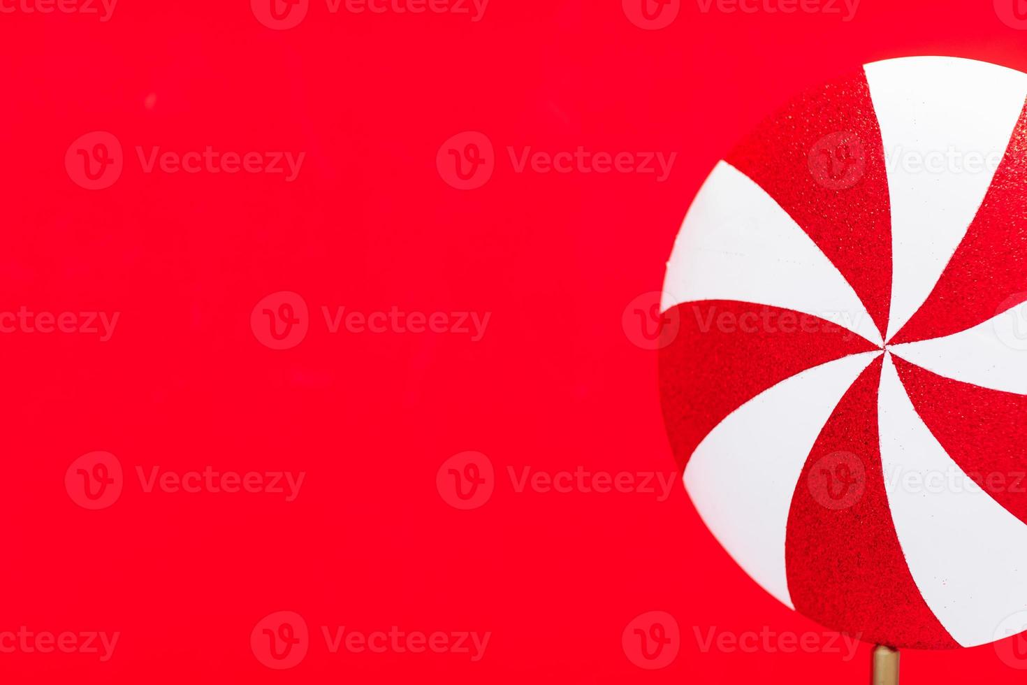 Red-white lollipop swirl on a white stick over red background. Top view, copy space. huge red and white candy. Sweetness. photo