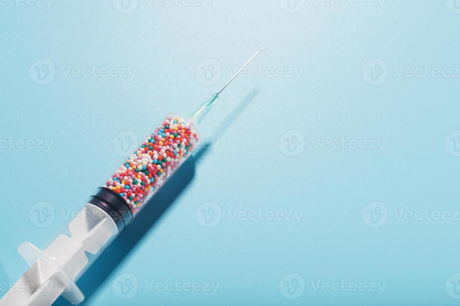 Syringe filled with colorful nano balls on a light blue background. photo