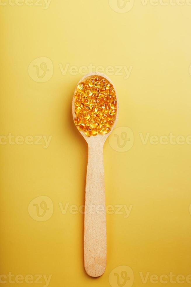 Vitamin D3 Capsules in a spoon with other vitamin D3 capsules around them on a yellow background photo