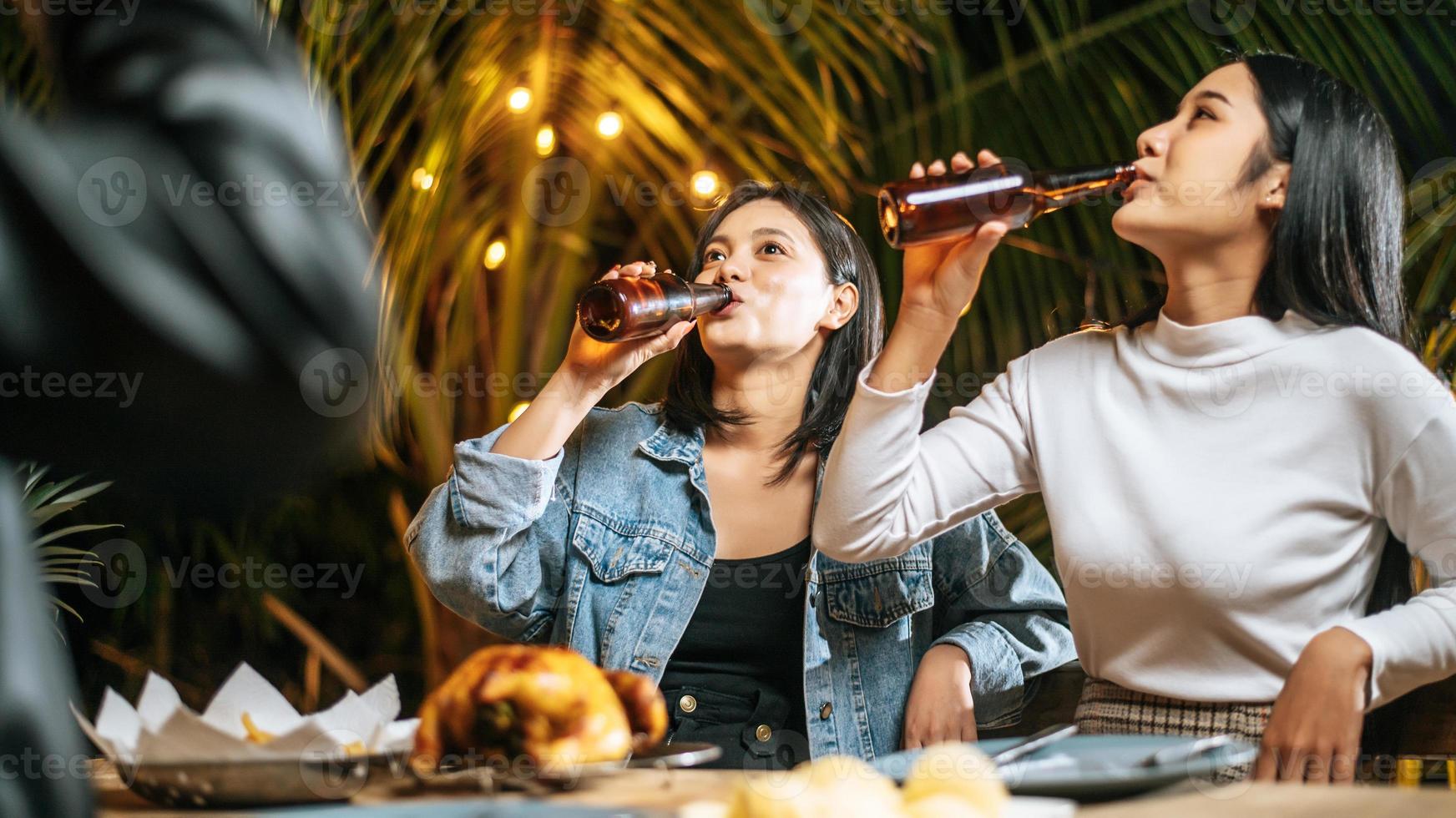 retrato de felices amigos asiáticos cenando juntos - jóvenes sentados en la mesa del bar brindando vasos de cerveza cenando al aire libre - gente, comida, estilo de vida de bebida, concepto de celebración de año nuevo. foto
