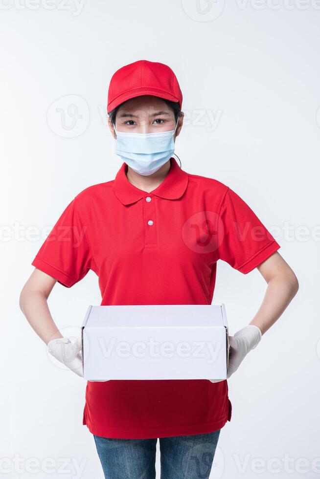 Image of a conscious young delivery man in red cap blank t-shirt uniform face mask gloves standing with empty white cardboard box isolated on light gray background studio photo