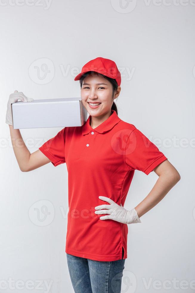 Image of  young delivery man in red cap blank t-shirt uniform standing with empty white cardboard box isolated on light gray background studio photo
