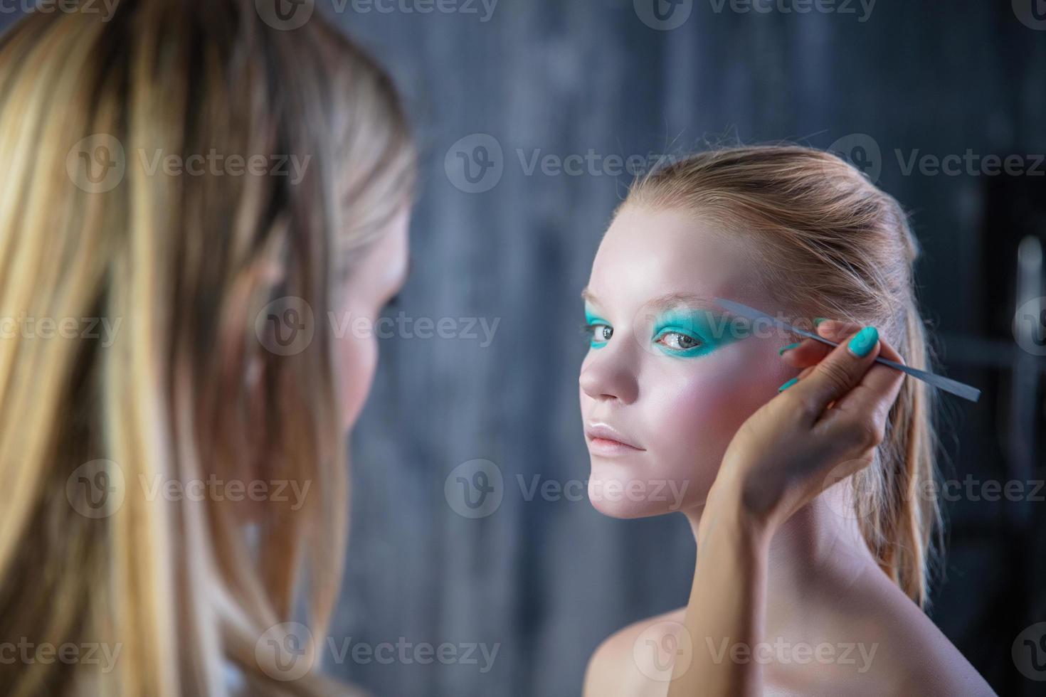 mujer aplica creativo maquillaje a el cara de un encantador joven modelo foto