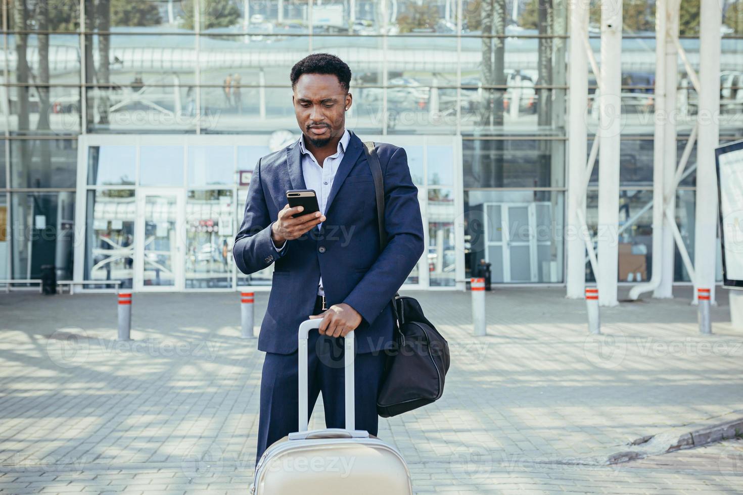 hombre de negocios africano que viaja cerca del aeropuerto con una maleta llamando a un taxi usando una aplicación móvil foto