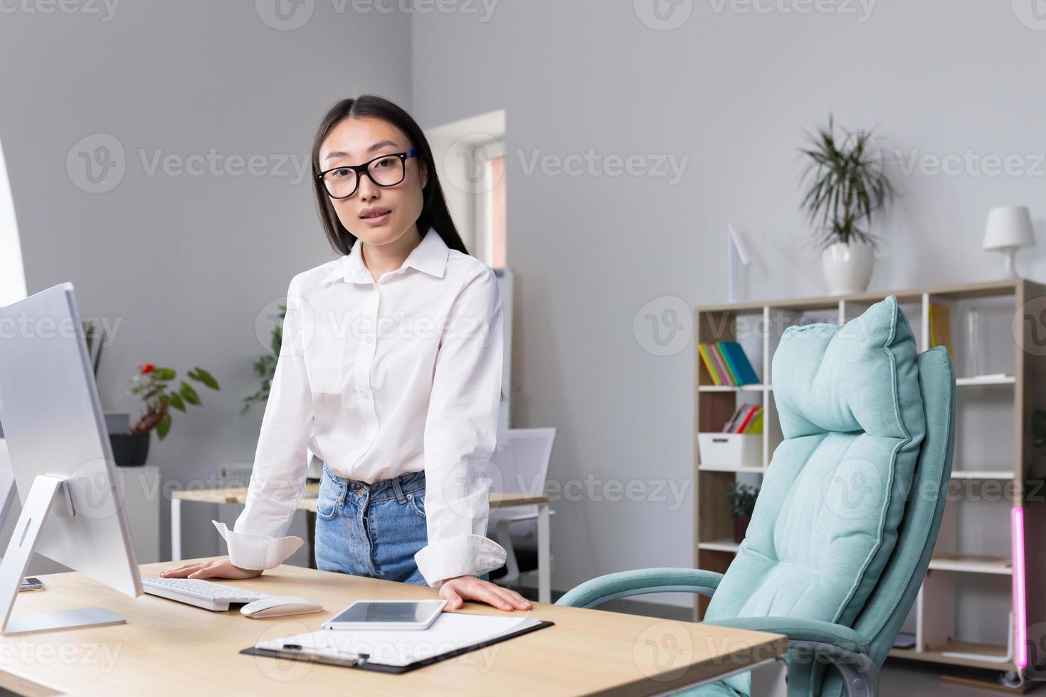 exitoso asiático negocio mujer a lugar de trabajo en oficina mirando a cámara, retrato de fuerte líder foto