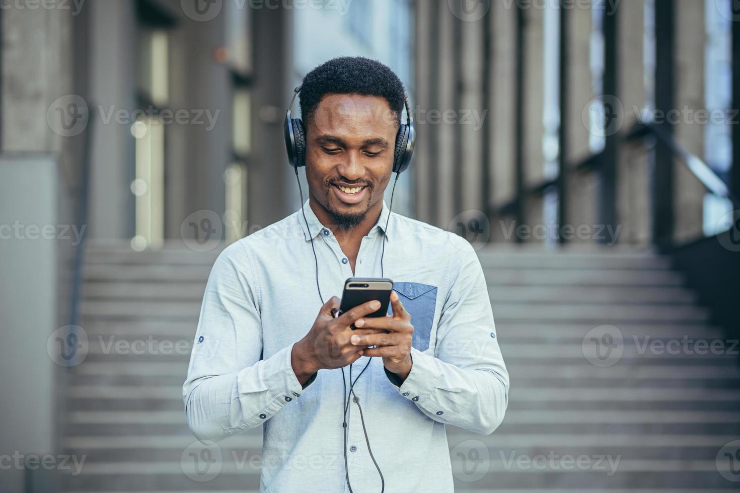 young african student listening to music from smartphone using big headphones photo