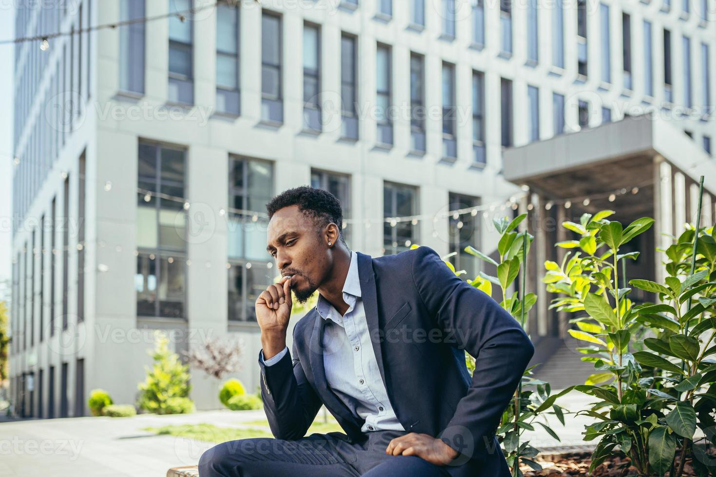 african american business man smoking cannabis outdoors sitting on city park bench photo