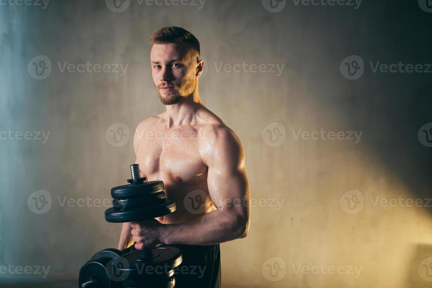 masculino rubio atleta ascensores pesas con mano en bíceps estudio foto con gotas de lluvia