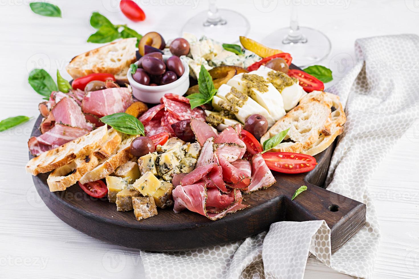 Antipasto platter with ham, prosciutto, salami, blue cheese, mozzarella with pesto and olives on a wooden background. photo