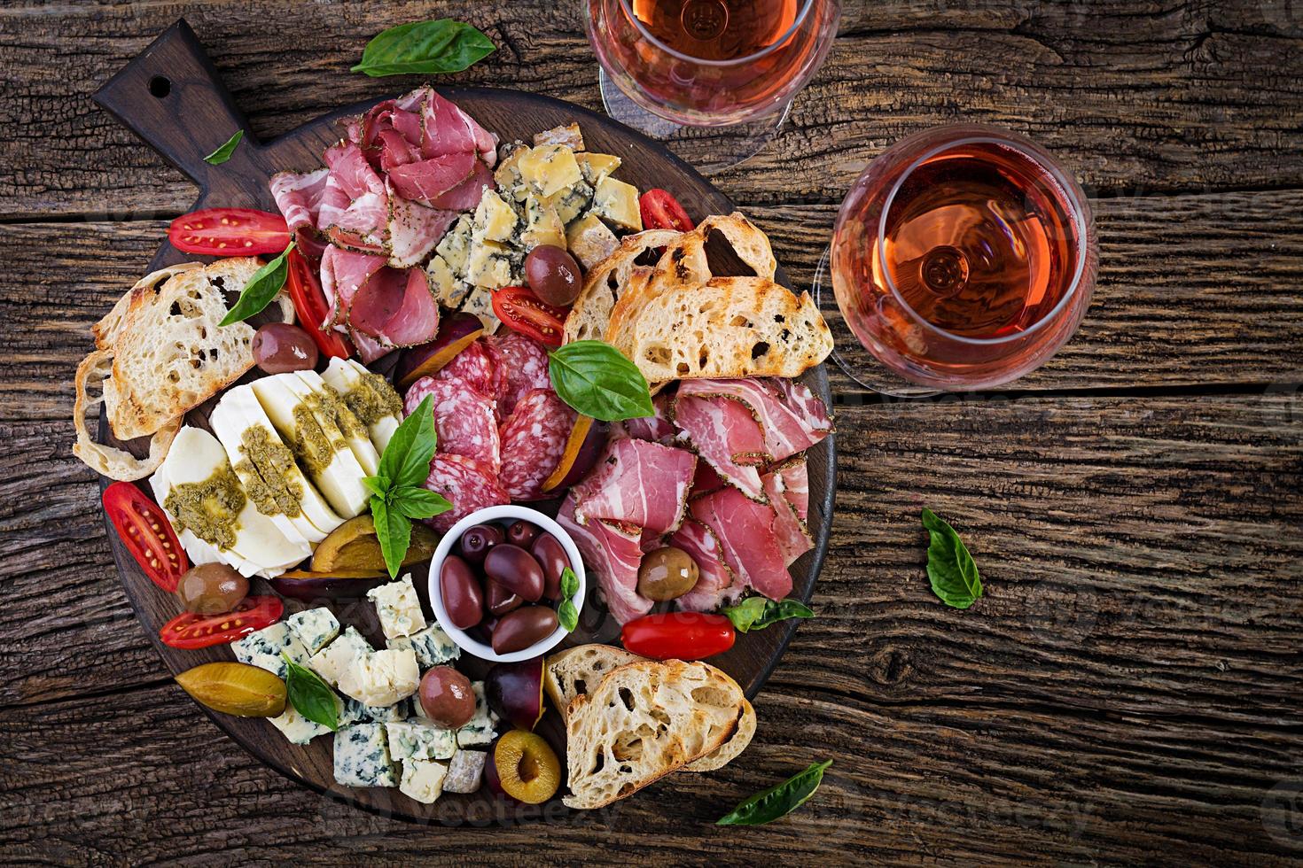 Antipasto platter with ham, prosciutto, salami, blue cheese, mozzarella with pesto and olives on a wooden background. Top view, overhead photo