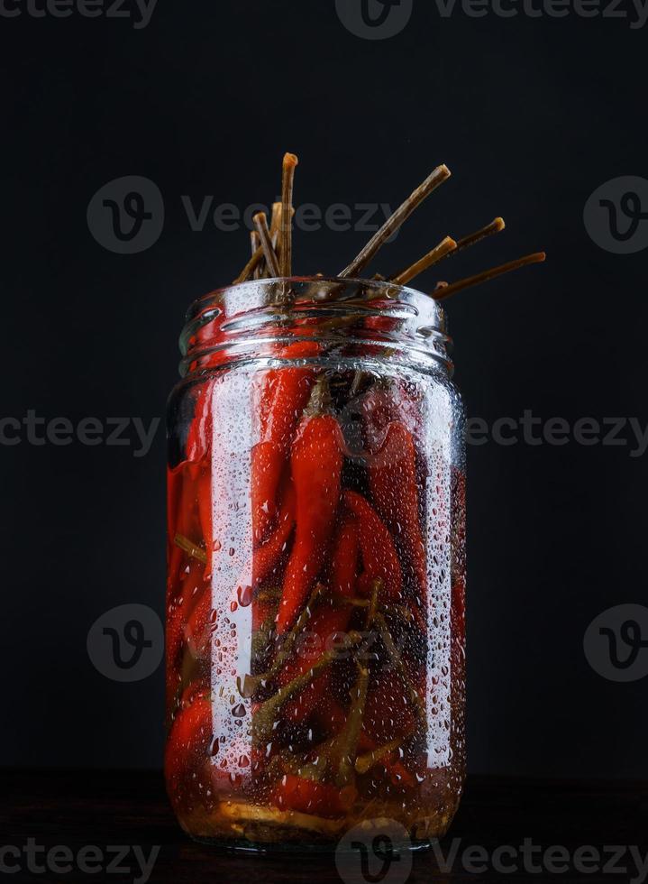 Frasco de vidrio con chiles en escabeche sobre fondo negro foto