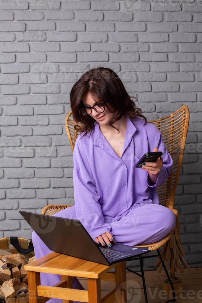 Beautiful businesswoman working on a laptop in a chair near the window. Female freelancer connecting to internet via computer. Blogger or journalist writing new article. photo