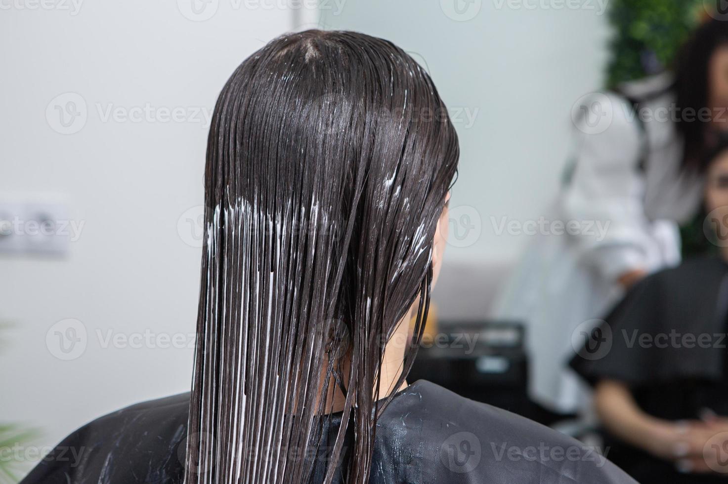 el peluquero aplica una máscara para el cabello al cabello negro liso. cuidado del cabello en el salón de belleza. foto