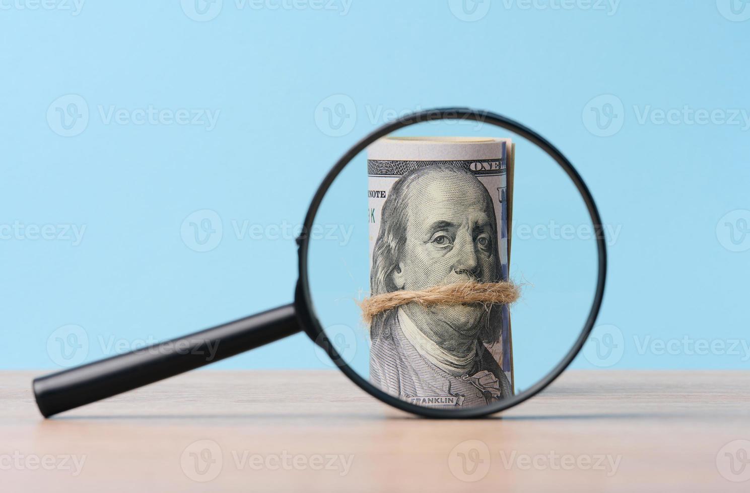 Plastic magnifying glass and bound roll of american dollars on blue background photo