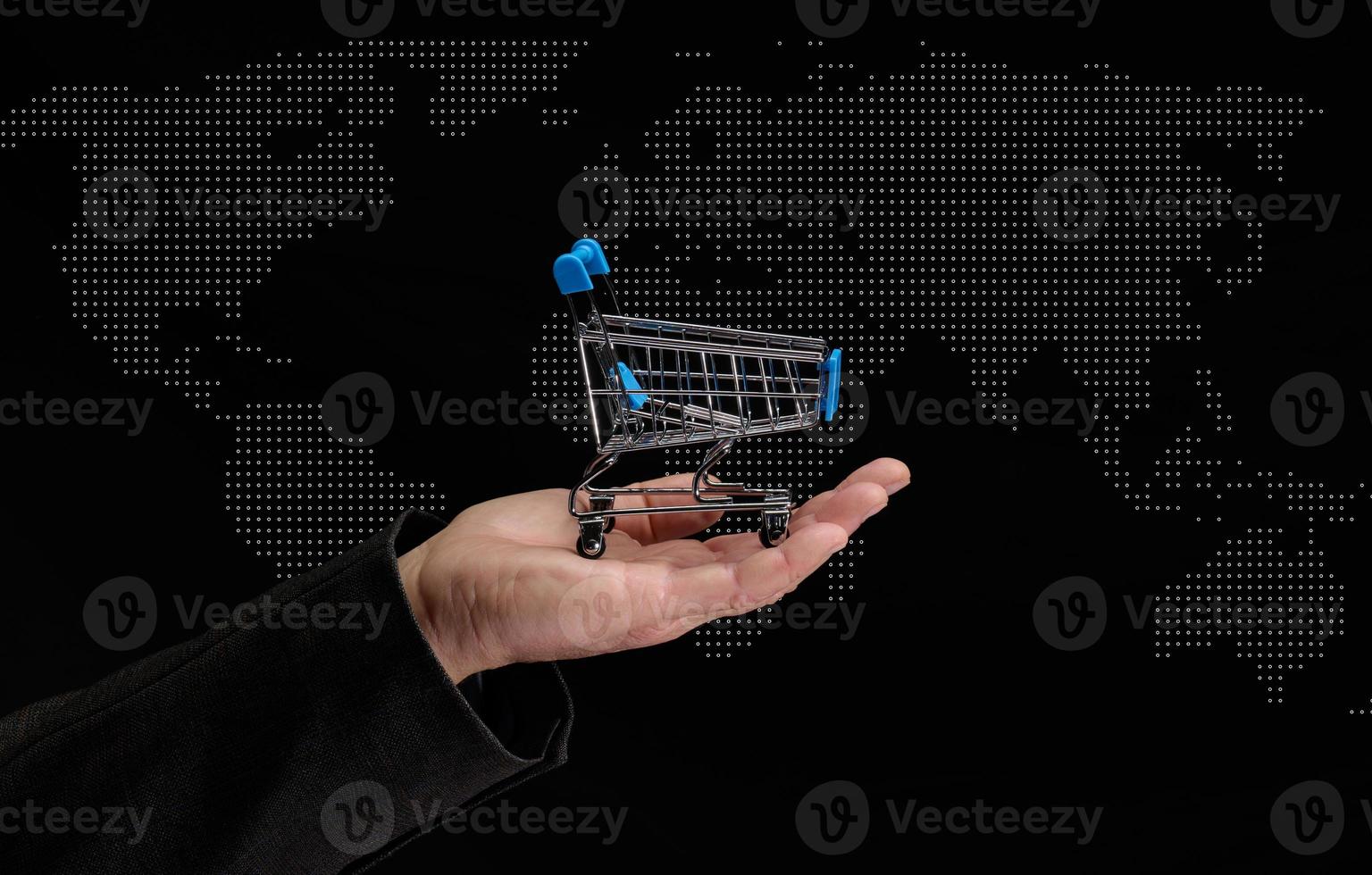 man's hand holds a miniature shopping cart on a dark background, concept of the start of world sales photo
