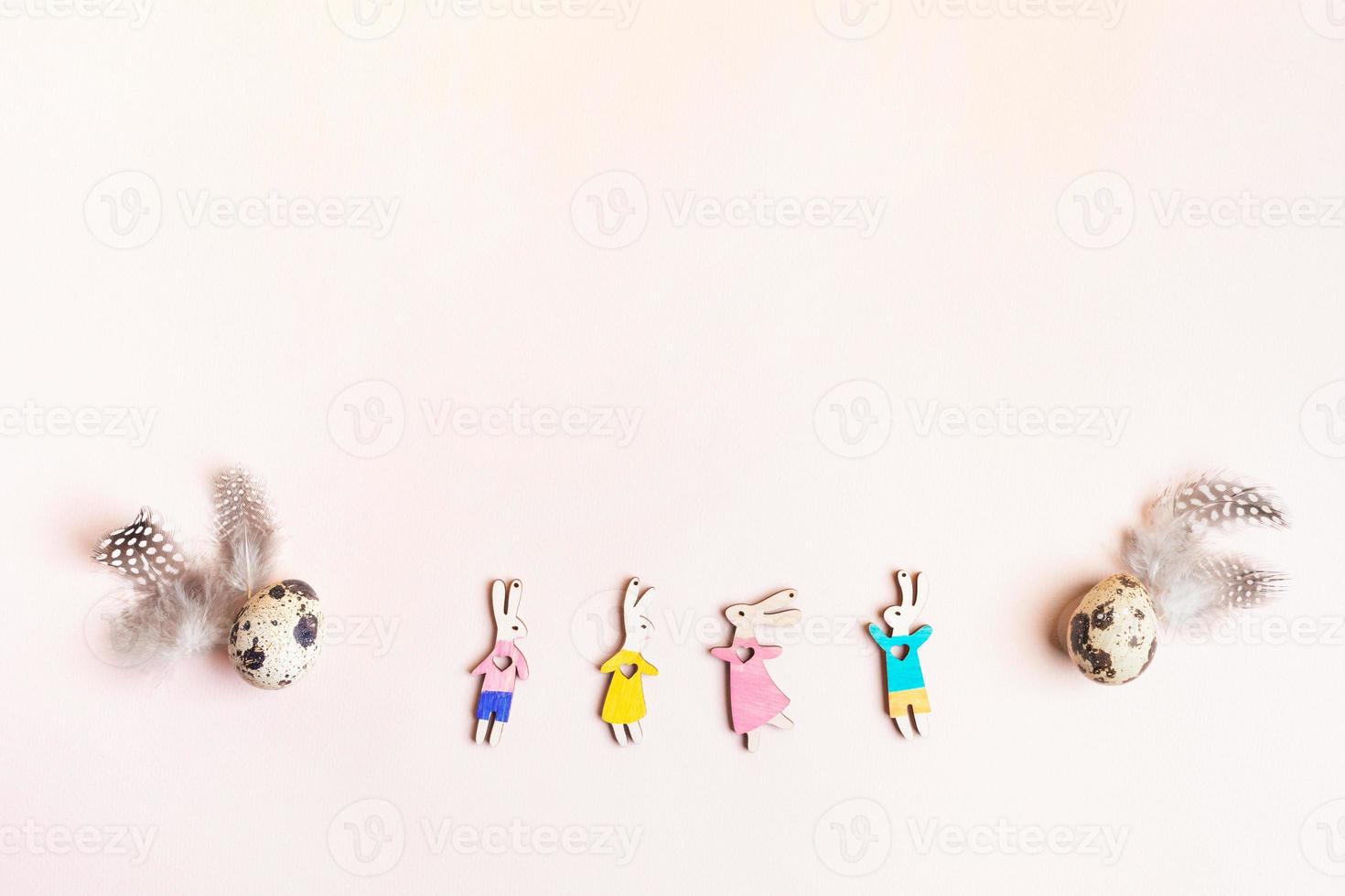 Colorful funny wooden bunnies, eggs, feathers as arc on pink. Easter image. Top view, copy space. photo