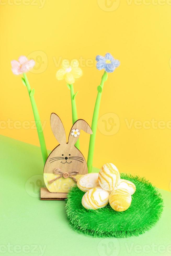 Wooden bunny, yarn flowers, round decorative grass carpet with textured Easter eggs on yellow-green. photo