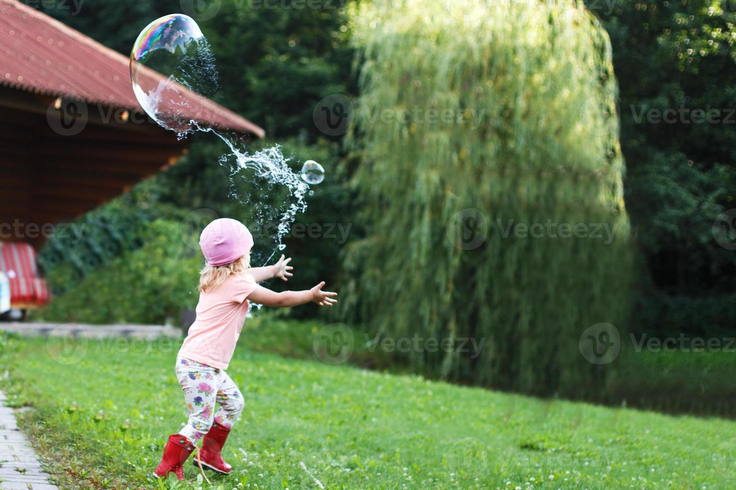 happy girl playing with soap bubbles outdoor. A little girl pops a soap bubble photo