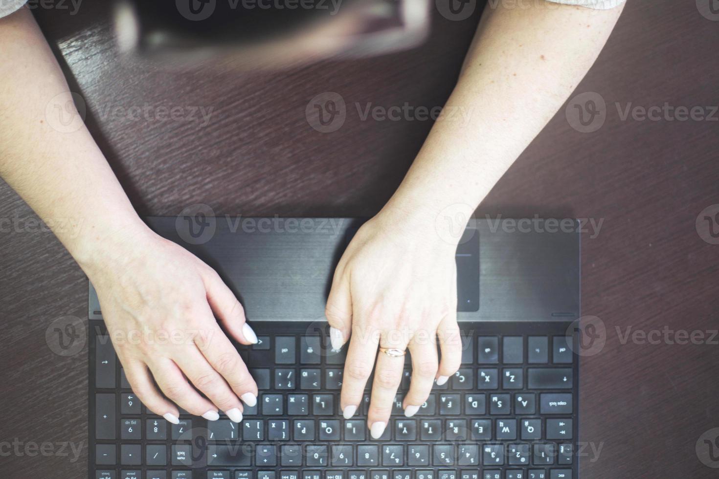 niña en el oficina es mecanografía en un ordenador portátil. niña a trabajar. niña manos en teclado cerca foto