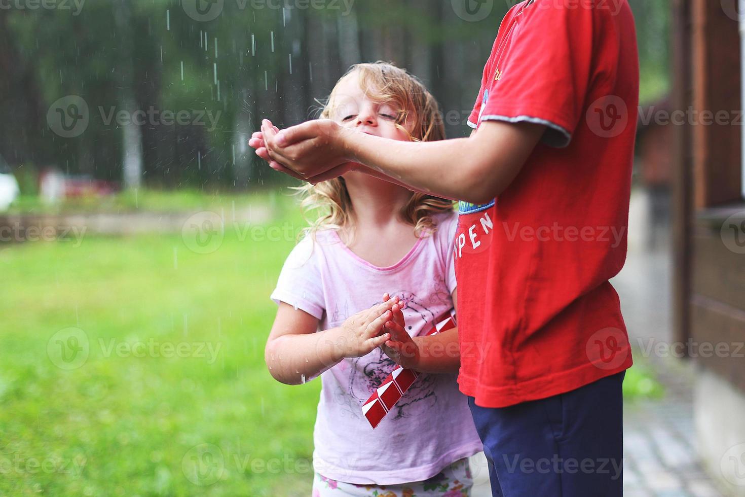 brother and sister play in rainy weather Children jump in puddle and mud in the rain. photo