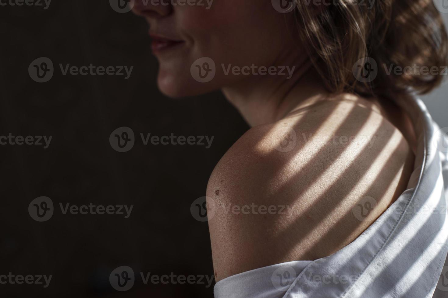 Sensual close up portrait of beautiful young lady relaxing at the window. female shoulder close up. hard shadows photo