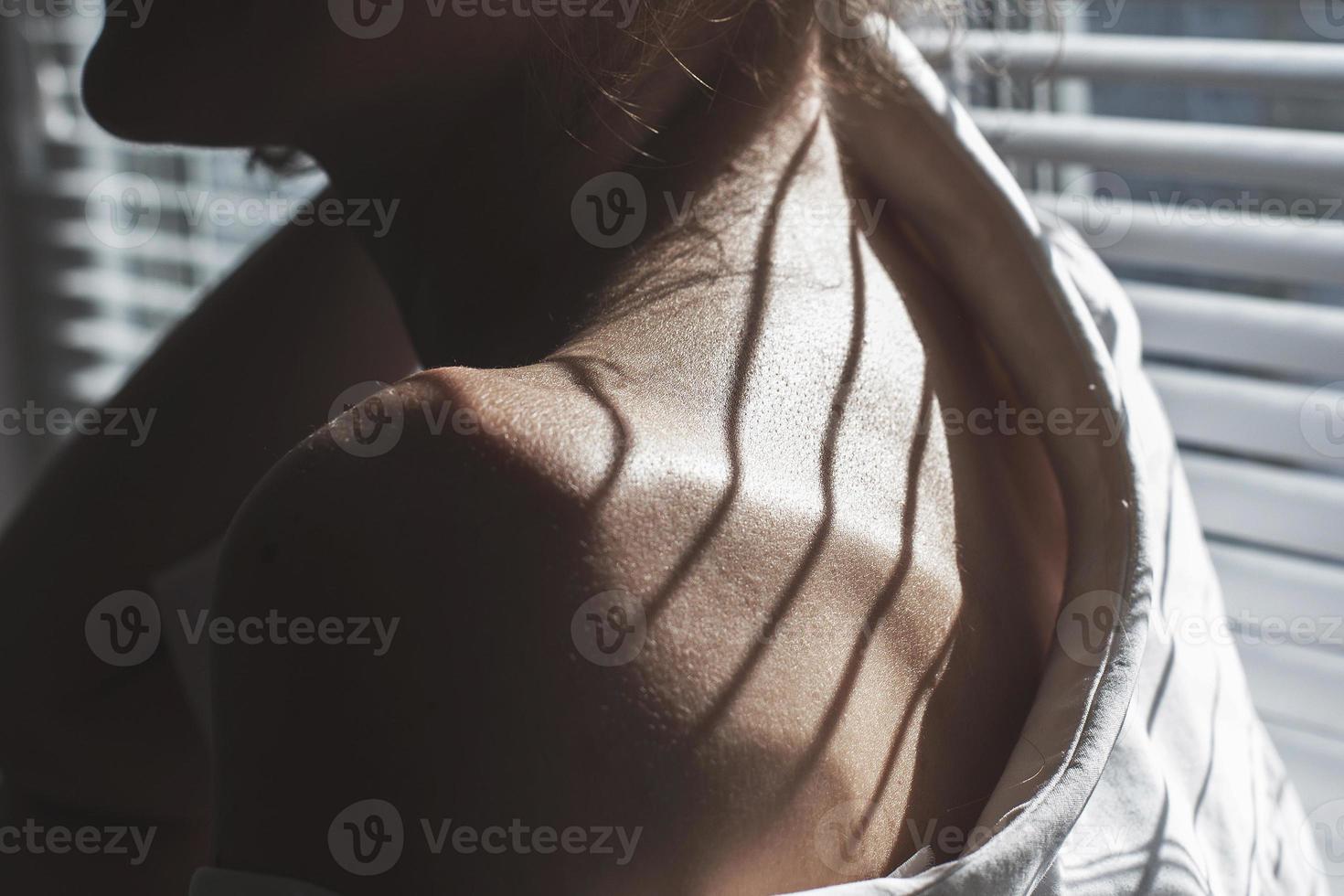 sensual cerca arriba retrato de hermosa joven dama relajante a el ventana. hembra hombro cerca arriba. difícil oscuridad foto