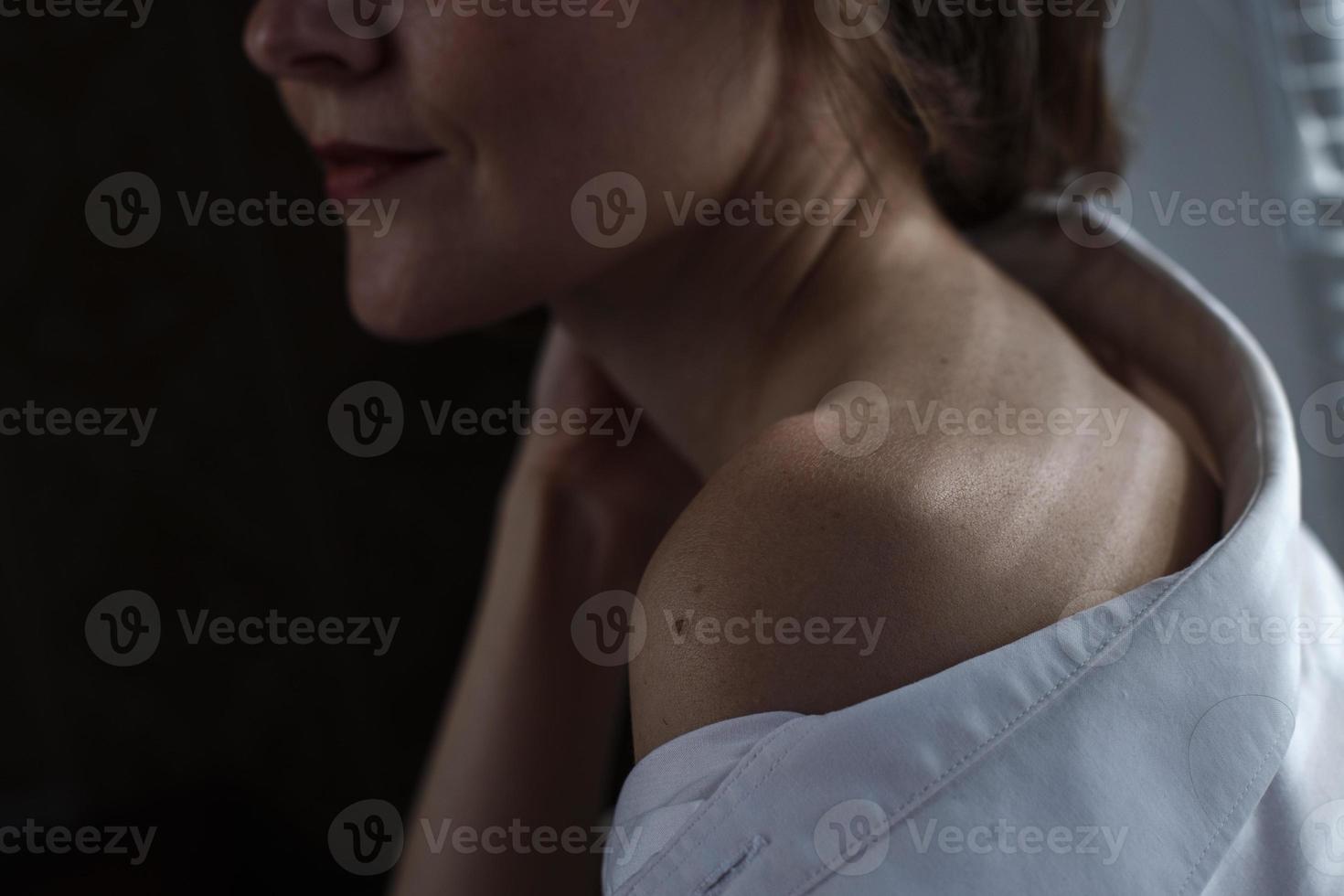 sensual cerca arriba retrato de hermosa joven dama relajante a el ventana. hembra hombro cerca arriba. difícil oscuridad foto