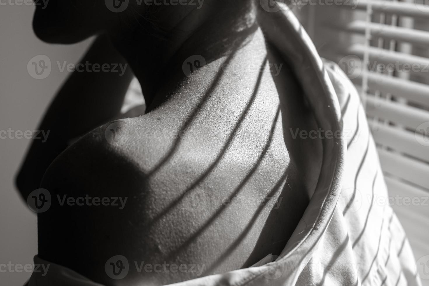 Sensual close up portrait of beautiful young lady relaxing at the window. female shoulder close up. hard shadows. photo