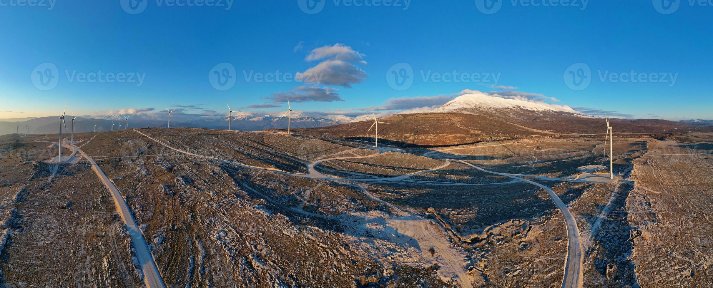 molinos de viento en las colinas durante la puesta de sol. energía renovable, energía verde. montañas en el fondo con nieve. energía eólica y respetuoso con el medio ambiente. Futuro sostenible. acabar con los combustibles fósiles. foto