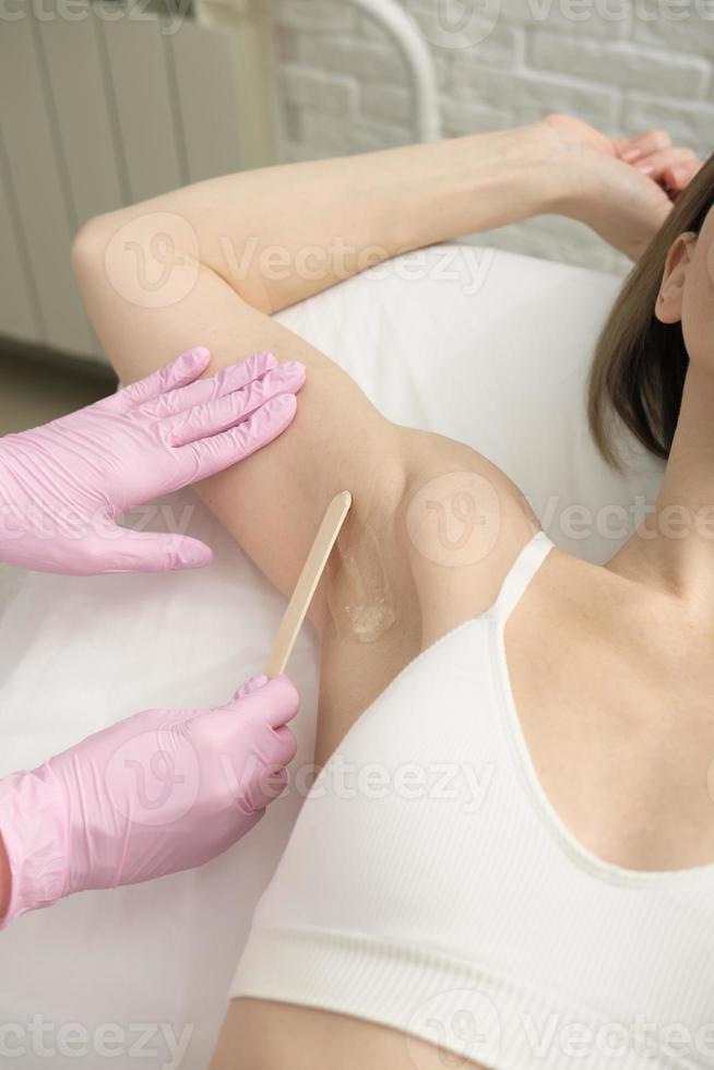 underarms depilation procedure, doctor applying guide gel with spatula on armpits of a client. photo