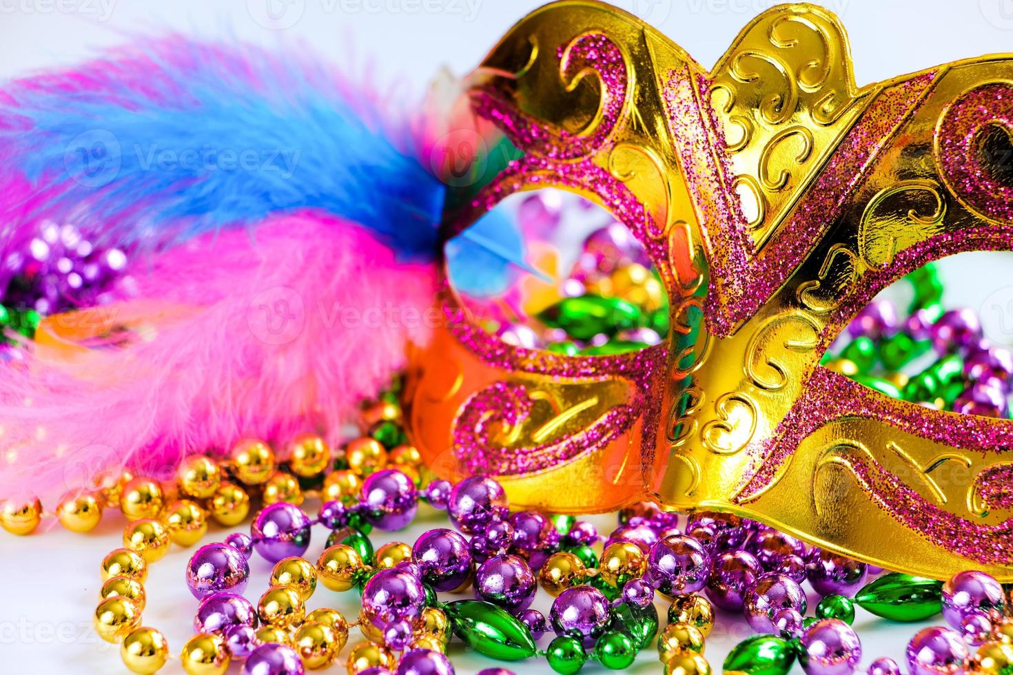 Golden carnival mask and colorful beads on white background. Closeup symbol of Mardi Gras or Fat Tuesday. photo