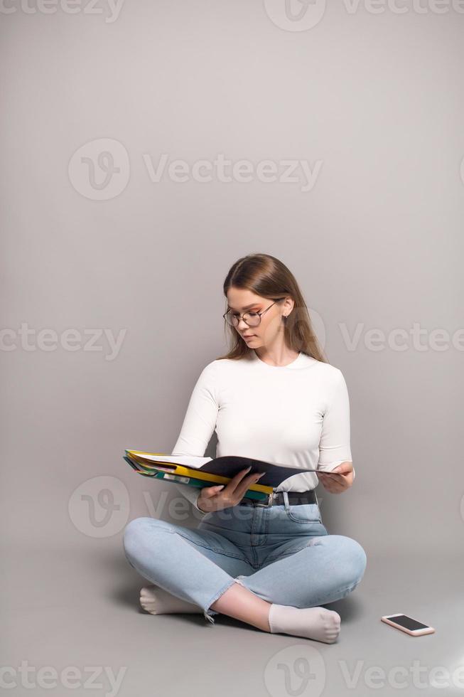 A cute student with glasses is sitting on a gray background and looking at folders for documents photo