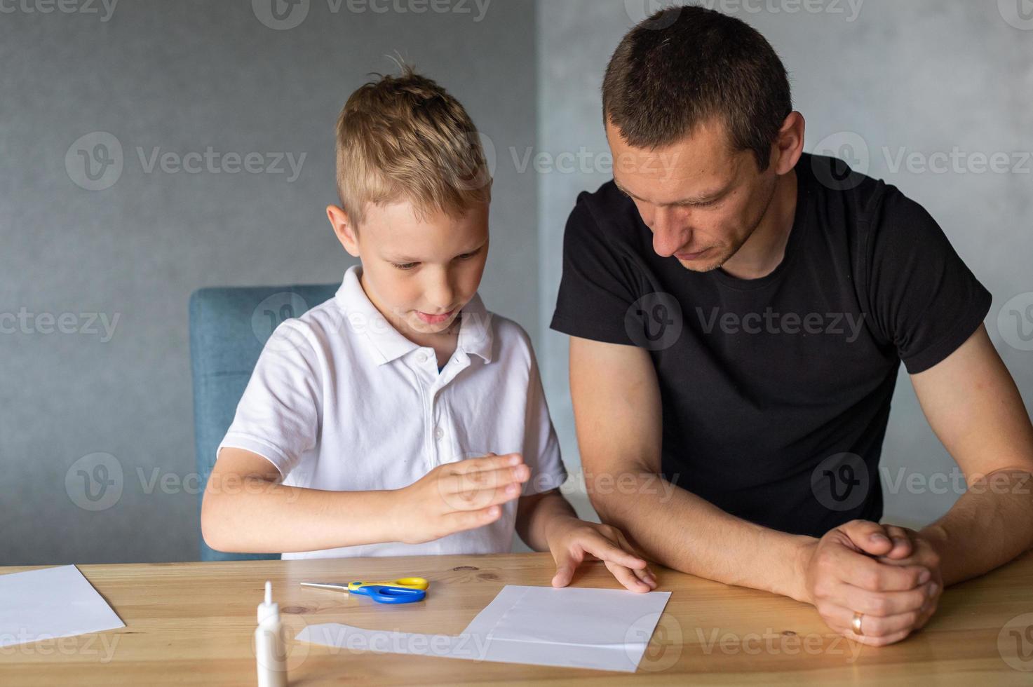 A cute boy is sitting with his dad at the table and collecting origami. Adds up the details photo