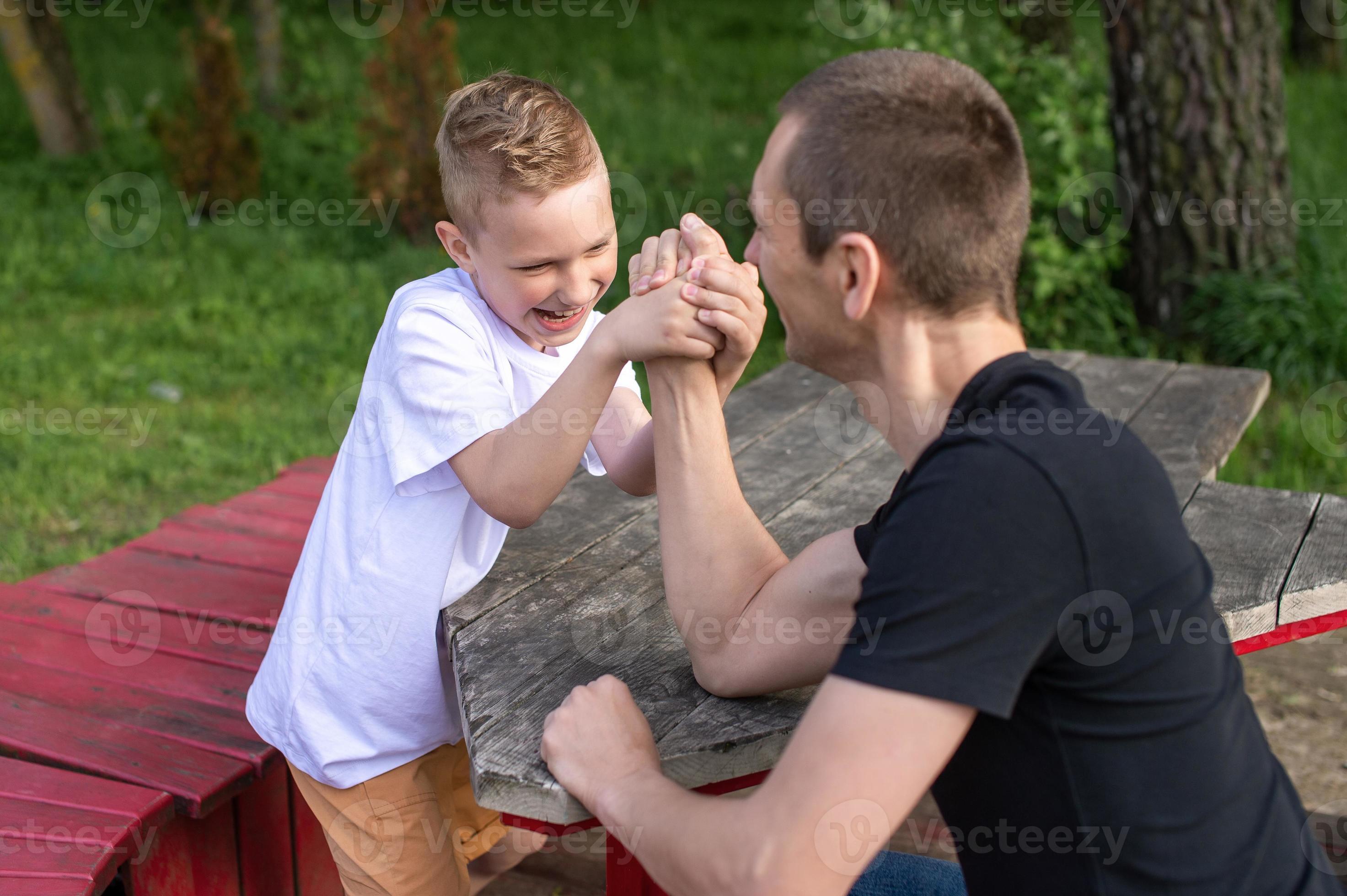A cute child tests the strength of his hands with his dad. Powerlifting