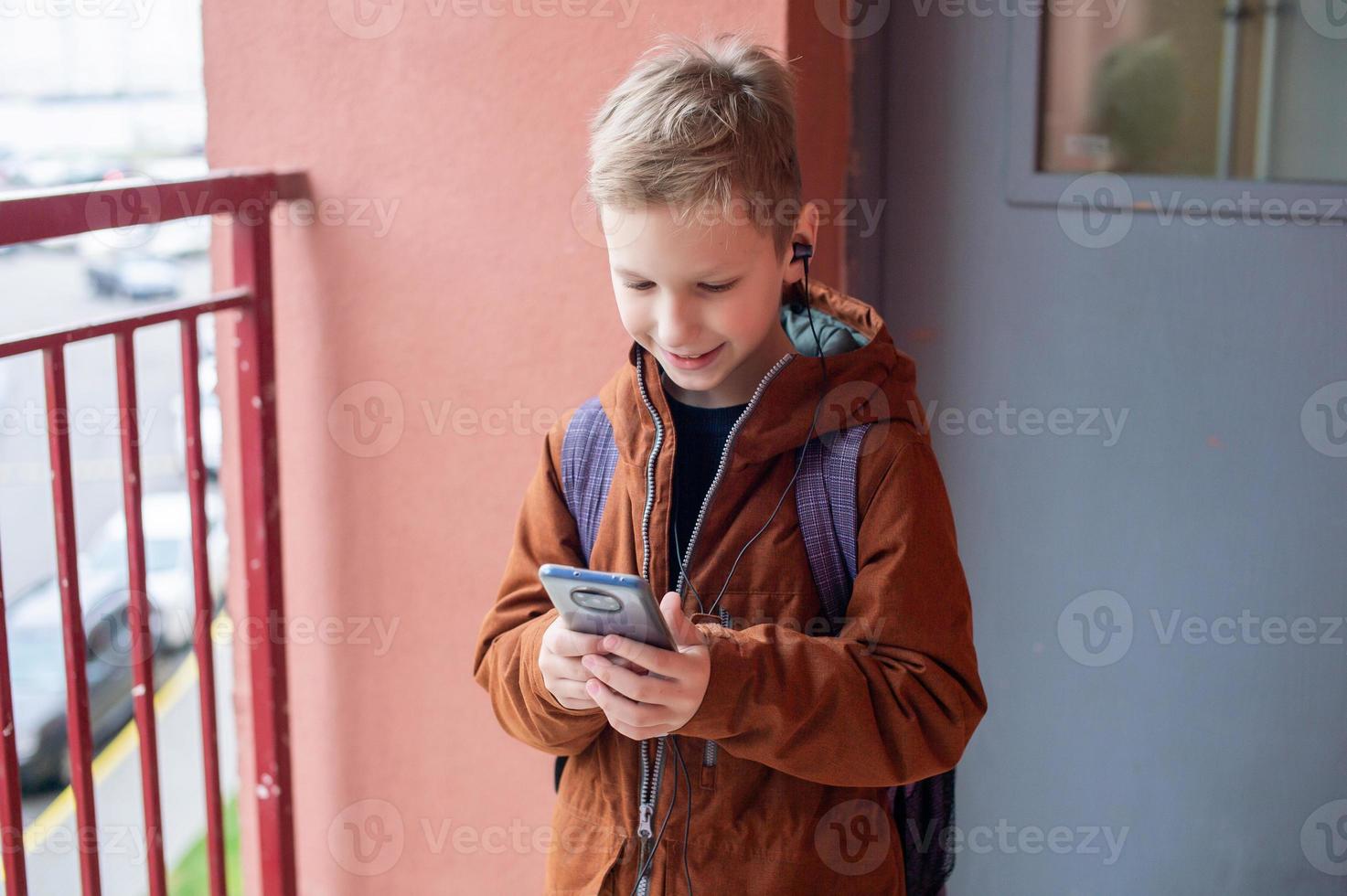 A cute boy is standing with a backpack and a phone with headphones photo