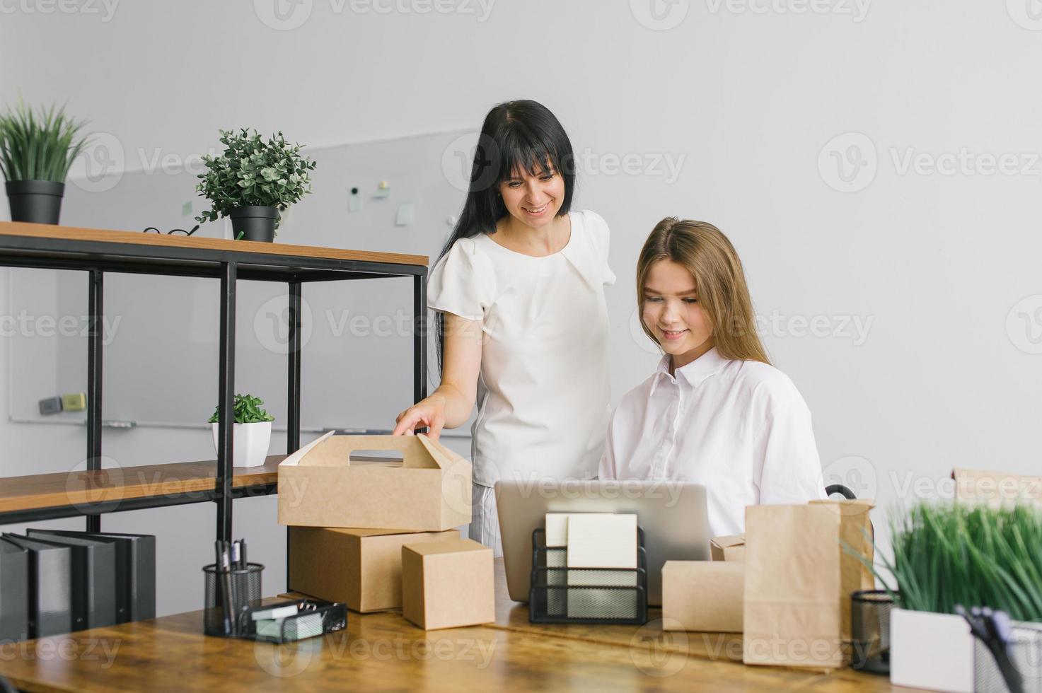 Two girls in the office are working with a laptop next to eco packages standing on the table photo
