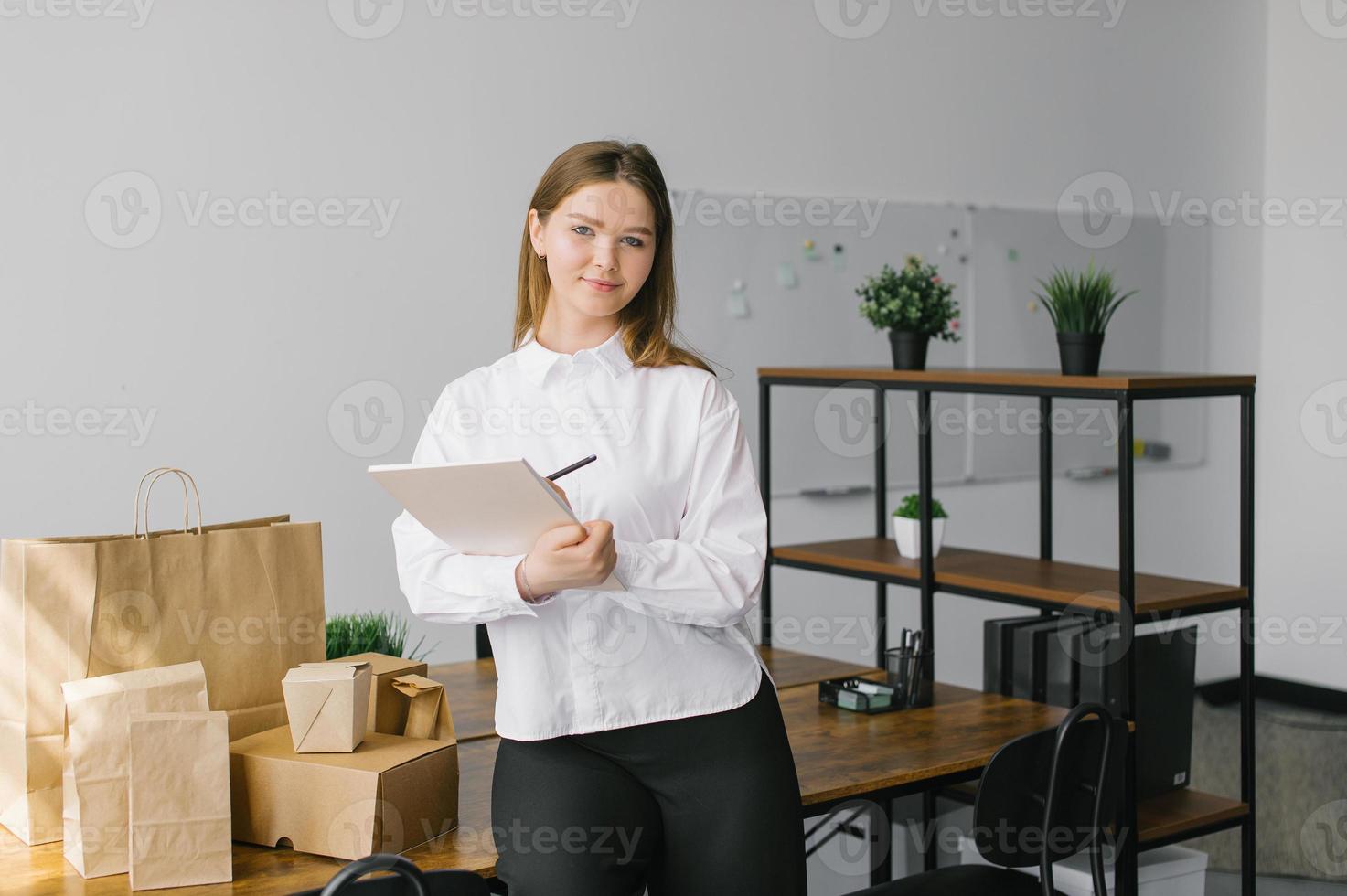 A cute girl with a notebook and looks at the eco packages standing on the desk in the office photo