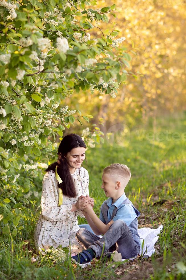 A mother with dark hair holds her son's hands and looks at him photo