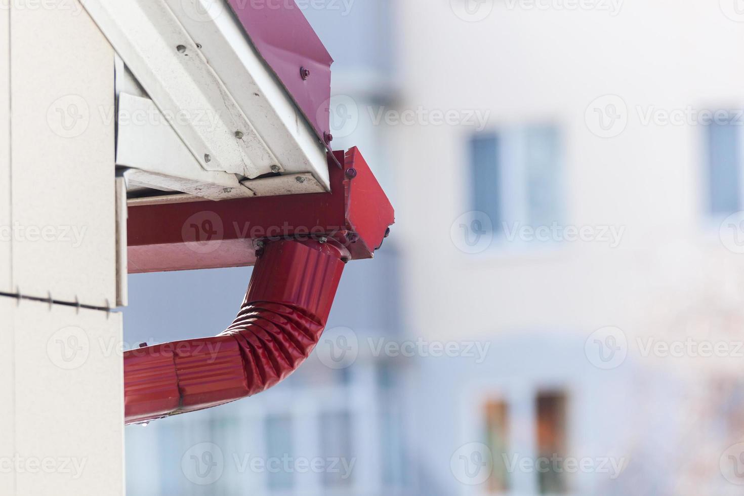 A drop of melting snow on the red roof gutter of a building against the background of a house. Photo in high quality. Horizontal.
