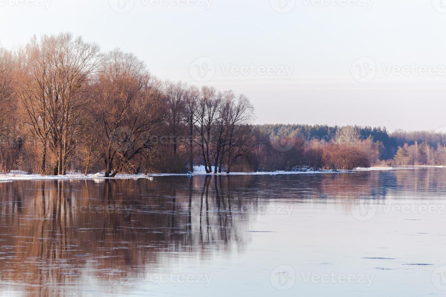 Spring on the river in the sunlight. Bare brown trees on the far bank of the river and remnants of snow. Background. High quality photo. Horizontal. Template. photo