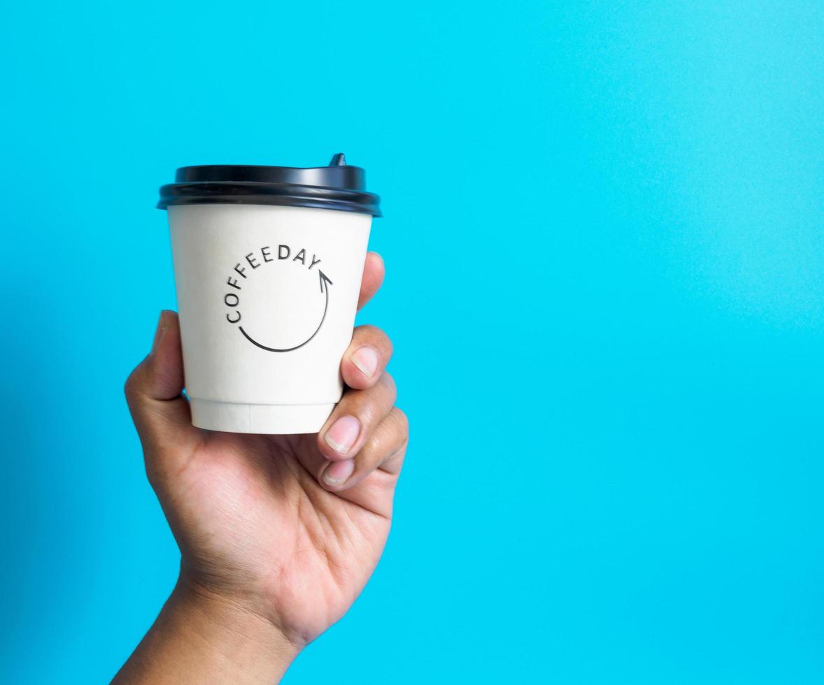 de cerca joven adulto hombre mano participación blanco taza papel de café caliente bebida Listo a bebida refrescante. aroma despierto Fresco a trabajo metido en un azul aislado antecedentes. punto de ver disparo. foto