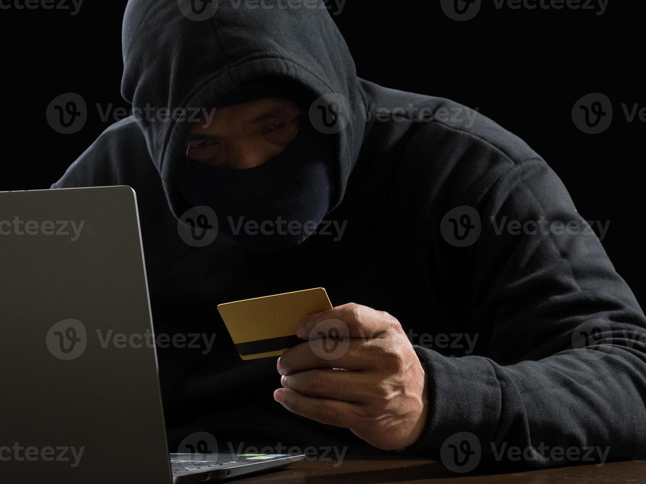 Hacker spy man one person in black hoodie sitting on a table looking computer laptop used login password attack security to circulate data digital in internet network system, night dark background. photo