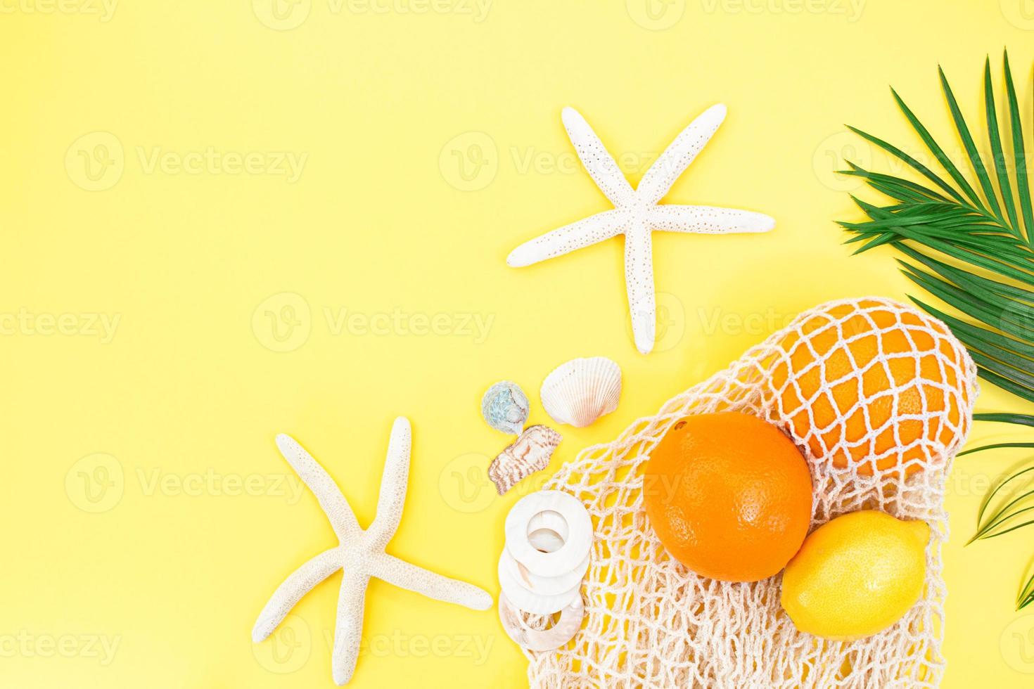 Starfish, shells with bag string bag with oranges and lemon with palm branch from the side on yellow background. Concept of summer time, vacation, travel. Copy space photo