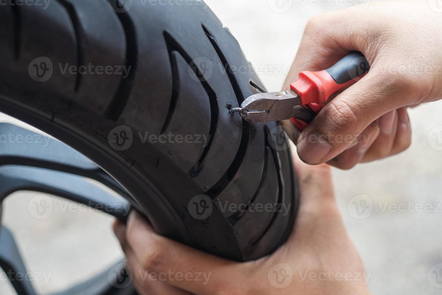 screw nail or Iron stuck puncturing motorcycle or scooter tire,mechanic repair a tire puncture from a nail or screw at motorcycle repair shop.motorcycle repair and maintenance concept photo