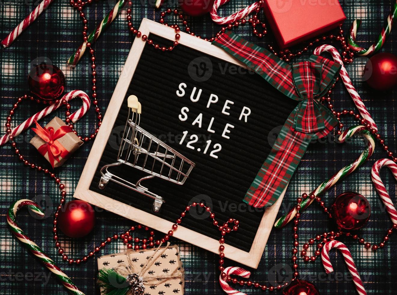 The text of the sale 12.12 on a letter board with a red gift box and Christmas candies, a credit card and a mini grocery cart. Design to promote the winter sale at the end of the year. Top view. photo