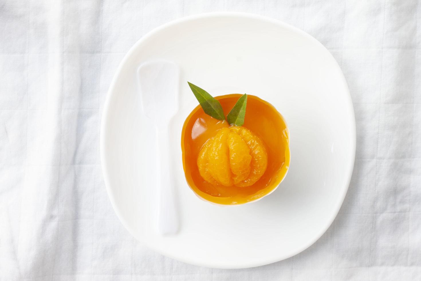 Top view of orange cupcake in paper cup on white plate with spoon for summer dessert on a tablecloth. photo